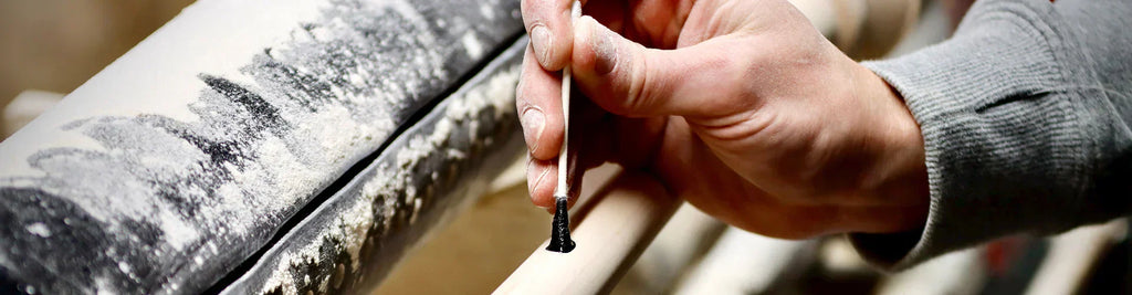 Close-up of craftsman applying ink dot test on wood baseball bat with cotton swab, checking grain slope for strength and safety.