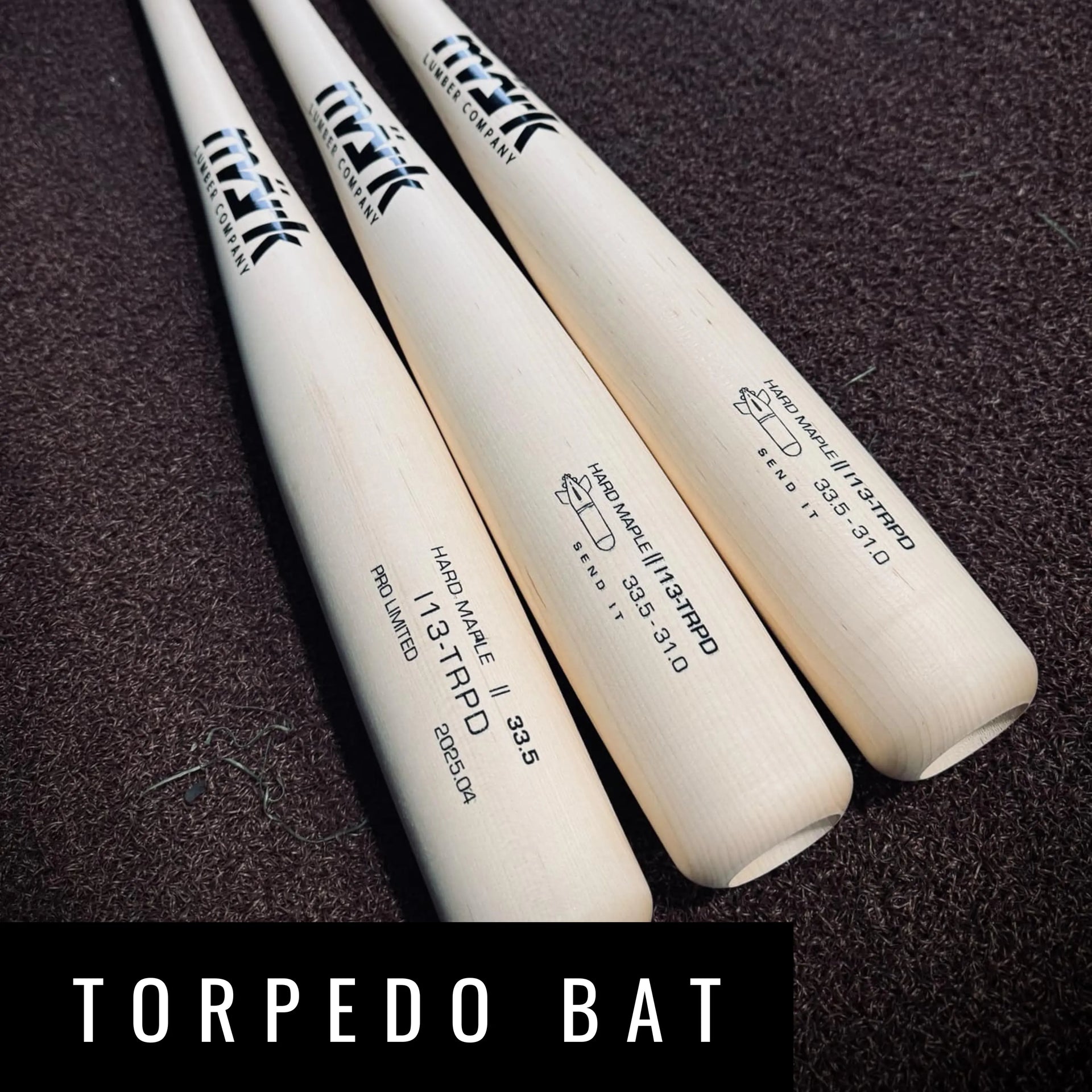 Three white handcrafted Mark Lumber Torpedo wood baseball bats in hard maple engraved with model 13‑TRPD on textured brown turf.