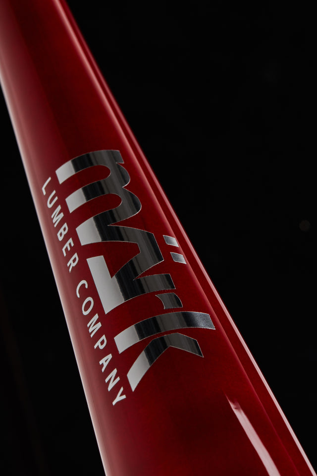 Close-up of a red Mark Lumber wood baseball bat barrel with the logo engraved on the surface.