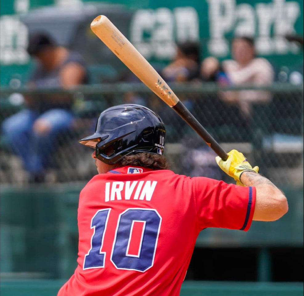 Baseball player in red jersey swings a MÄRK Lumber wood bat during a game, showcasing premium maple bat performance.