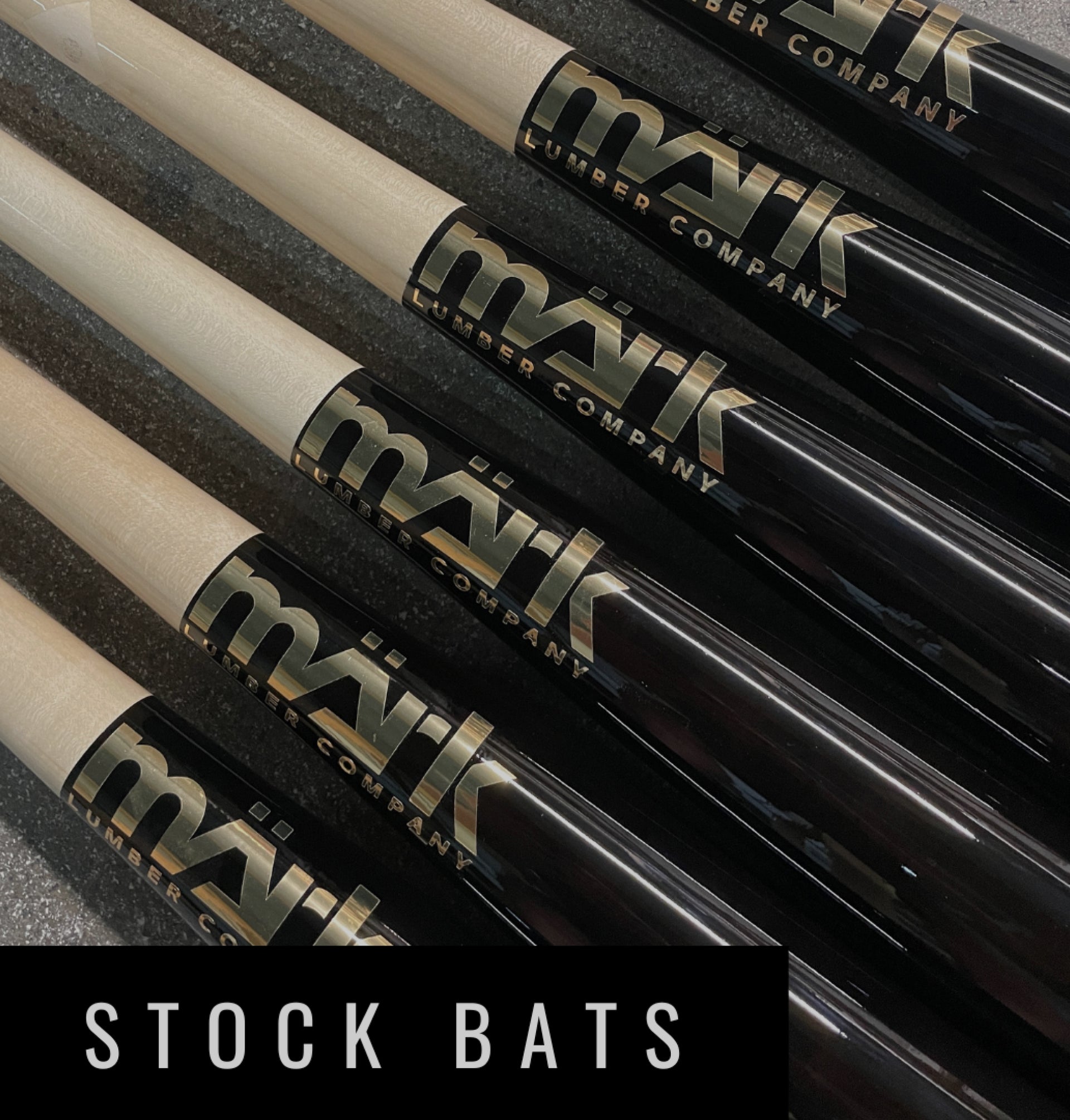 Close-up of Mark Lumber stock wood baseball bats with black barrels and natural maple handles, showing the bold Mark logo.