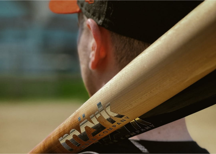 Baseball player resting a Märk Lumber Company wood baseball bat on his shoulder during practice, showcasing premium craftsmanship.