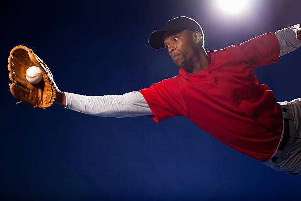 Baseball player in a red uniform making a full-stretch diving catch with a glove under stadium lights.